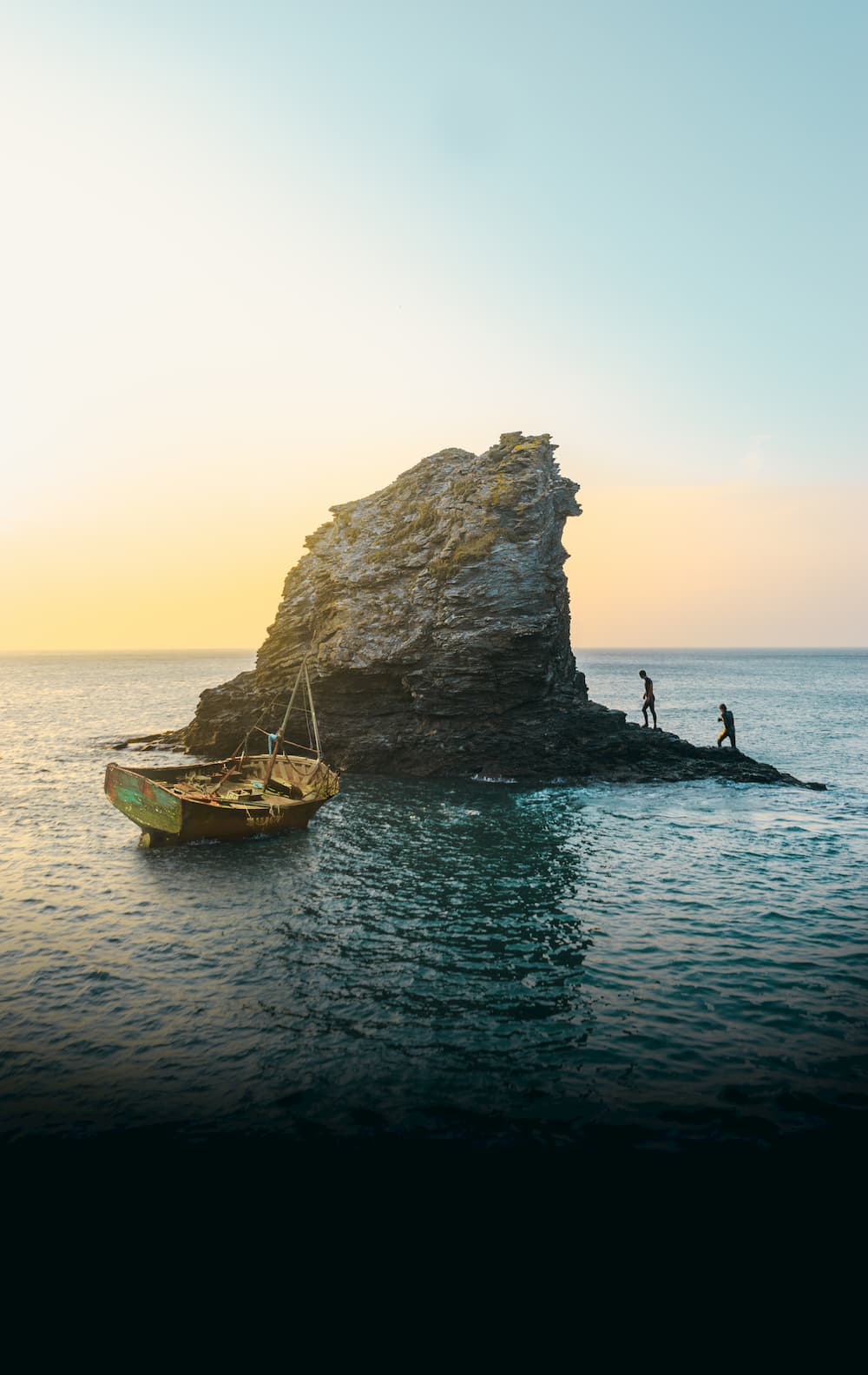 Image of two people climbing an island in the middle of a body of water with a boat docked at the shore